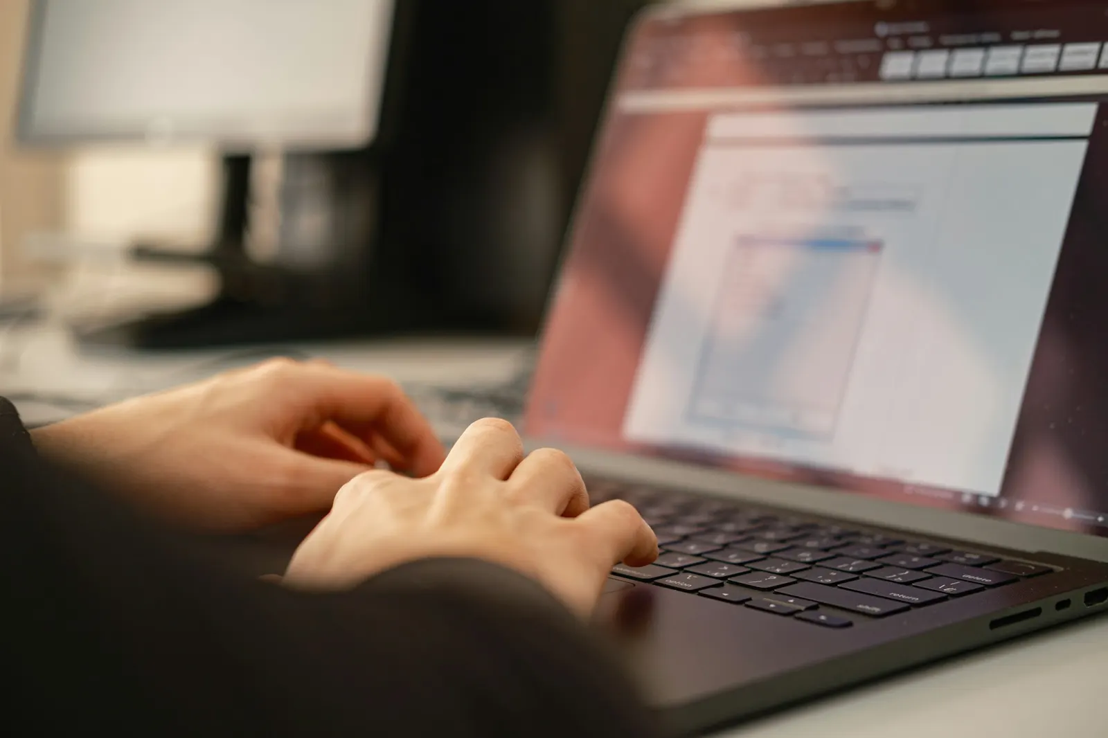 Hands typing on a laptop at a desk